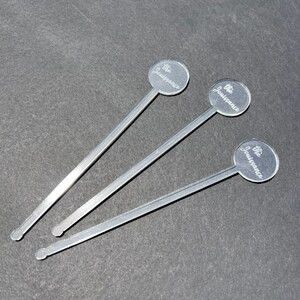 May include: Three silver stirring sticks with round, clear tops. Each top has the words "The Jouissance" engraved on it.