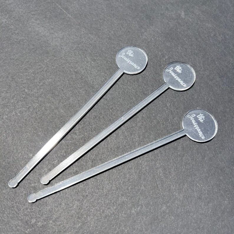 May include: Three silver stirring sticks with round, clear tops. Each top has the words "The Jouissance" engraved on it.