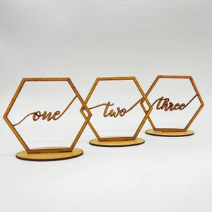 May include: Three wooden hexagonal table number holders with the words "one", "two", and "three" written in cursive script.