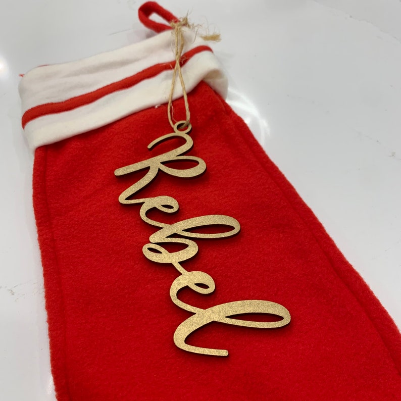 May include: A red stocking with a white cuff and a gold wooden ornament that says "blessed" hanging from it.