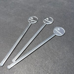 May include: Three silver stirring sticks with round, clear tops. Each top has the text "The Jouissance" engraved on it.