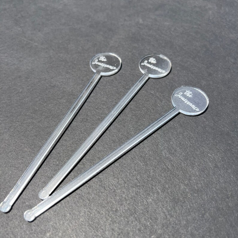 May include: Three silver stirring sticks with round, clear tops. Each top has the text "The Jouissance" engraved on it.
