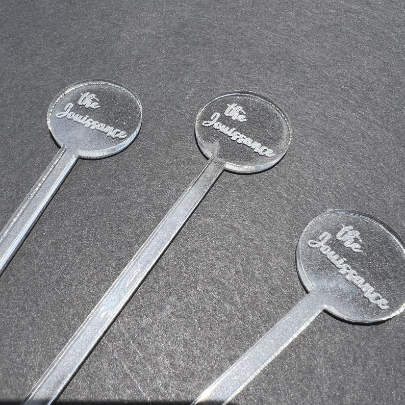 May include: Three clear acrylic cocktail stirrers with round tops. Each top has the text "the Jouissance" engraved on it.