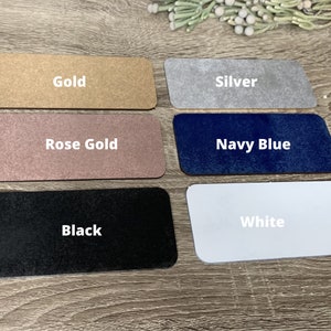 May include: Five rectangular samples of different colours: gold, silver, rose gold, navy blue, and white. The samples are arranged in two rows, with the gold and silver samples in the top row and the rose gold, navy blue, and white samples in the bottom row.