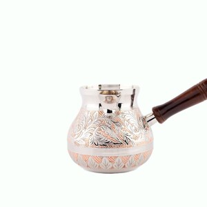 May include: A silver and copper Turkish coffee pot with a wooden handle. The pot has an intricate floral design.