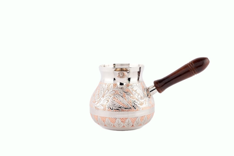 May include: A silver and copper Turkish coffee pot with a wooden handle. The pot has an intricate floral design.