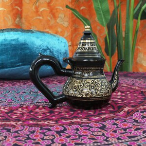 May include: A black metal teapot with gold floral designs. The teapot has a round body and a curved spout. The handle is black and has a curved shape.