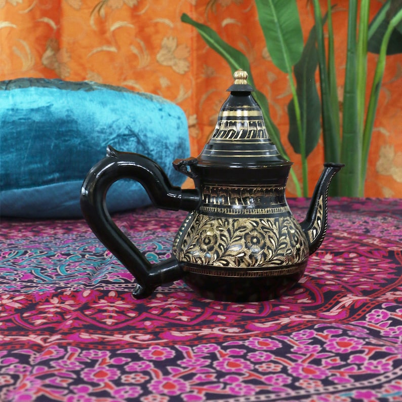 May include: A black metal teapot with gold floral designs. The teapot has a round body and a curved spout. The handle is black and has a curved shape.