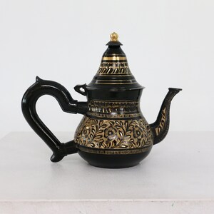 May include: Black teapot with a gold floral design and a gold lid. The teapot has a curved spout and a handle.