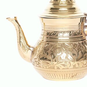 May include: A gold-colored metal teapot with an ornate floral design. The teapot has a lid and a spout.