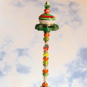 May include: A colorful glass bead and ceramic topped garden stake with a green base and a clear glass bowl filled with blue and green glass stones.