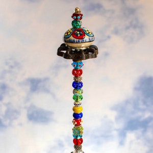 May include: A colorful glass bead and ceramic floral design topped decorative piece with a glass bowl filled with glass beads.