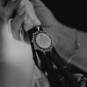 May include: A black and white image of a bouquet with a decorative pendant. The pendant is round with a floral border and contains text. The text reads: "Gabe I couldn't say I do without you. Thank you for being my bridesmaid..." and the date 06.26.21.