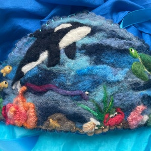 May include: A felt wall hanging depicting an underwater scene with an orca, a sea turtle, coral, and seaweed. The background is a blue and green gradient.
