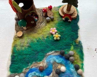May include: A felt play mat with a green and blue landscape, a brown tree trunk with a door, a green tree, a rainbow, and a flower. There are also small felt balls in various colors scattered around the mat.