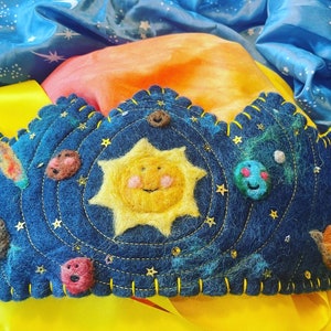 Op de afbeelding: Een blauwe viltkroon met een gele viltzon en planeten in het midden. De kroon is versierd met gouden sterren en pailletten.
