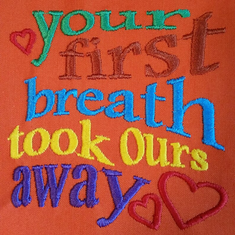 Puede incluir: Tela naranja bordada con el texto "your first breath took ours away" en colores arco&iacute;ris con un coraz&oacute;n al principio y al final del texto.