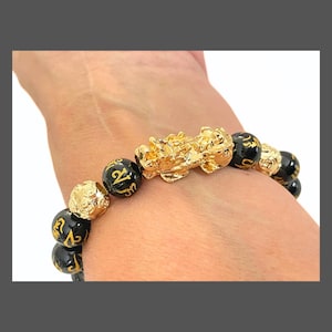 May include: A black and gold bracelet with a gold dragon charm and black beads with gold lettering. The bracelet is on a person's wrist.