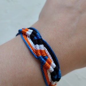 May include: A woven friendship bracelet with blue, orange, white, and black threads.