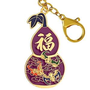 May include: A gold-colored metal keychain with a purple gourd-shaped charm. The charm features the Chinese character "Fu" in gold, along with illustrations of bats and clouds. The keychain has a lobster clasp for easy attachment.