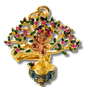 May include: A gold-colored ring featuring a detailed miniature tree design. The tree has pink and yellow fruit, green leaves, and a small monkey figure. The base of the tree is a blue and gold decorative pot.