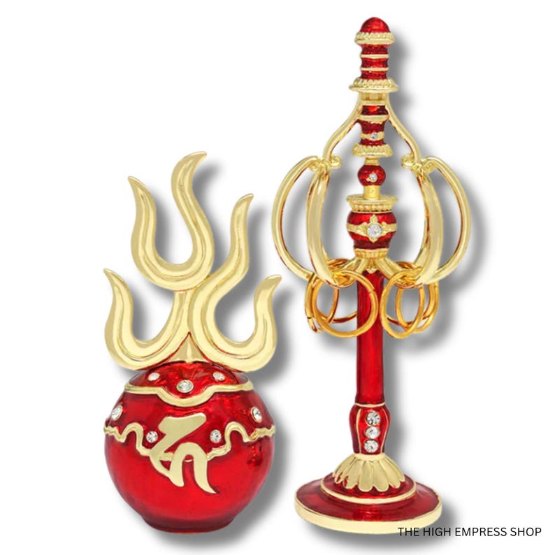 May include: Two ornate decorative objects. One is a red and gold sphere with a gold flame design on top. The other is a red and gold stand with gold rings and decorative elements. Both have jewel accents.