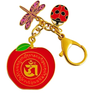 May include: A gold-colored keychain with a red apple charm featuring gold lettering and a green leaf. The keychain also includes a dragonfly and ladybug charm, connected by a gold chain and clasp.