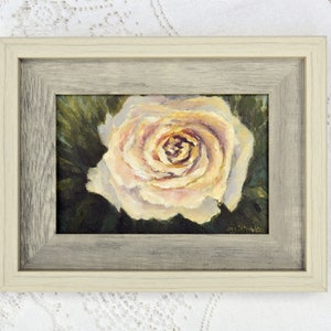 May include: A framed painting of a single, pale pink rose with a dark green background. The rose is in focus and the background is blurred. The painting is signed "JM Smith" in the bottom right corner.