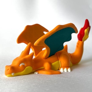 May include: A vibrant orange dragon figurine with yellow accents on its belly and face, and white claws. The dragon has orange wings with teal undersides and a red and yellow flame at the tail.