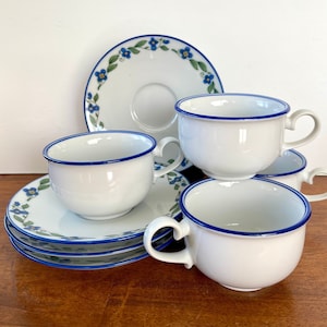 May include: Set of four white teacups and saucers with a blue and green floral pattern. The cups have a blue rim and the saucers have a blue and green floral border.