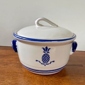 May include: White ceramic casserole dish with a blue and white pineapple design. The dish has two blue handles and a lid with a knob.