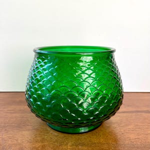 May include: A vibrant green glass bowl with a textured, scale-like pattern. The bowl has a rounded shape with a slightly flared rim and sits on a small, circular base. The glass is a deep, rich green color.