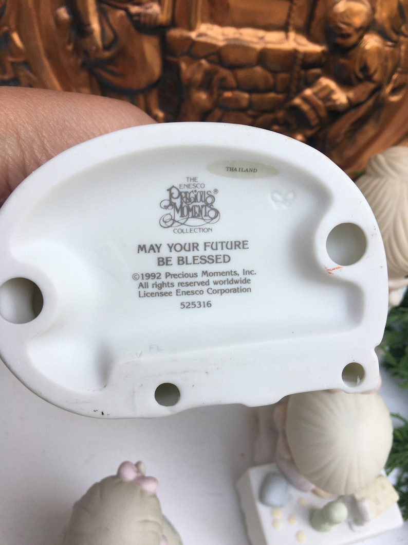Puede incluir: Una figurita de porcelana blanca de una ni&ntilde;a que sostiene un ramo de flores. La figurita es parte de la colecci&oacute;n Precious Moments y tiene la inscripci&oacute;n "Que tu futuro sea bendecido".