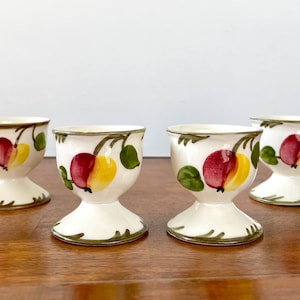 May include: Set of four white ceramic egg cups with a green, red, and yellow apple design.
