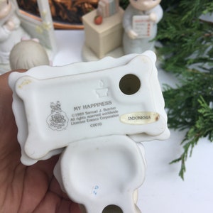Puede incluir: Figurilla de porcelana blanca de una ni&ntilde;a sosteniendo una almohada con las palabras "My Happiness" en ella. La figurilla est&aacute; hecha por Precious Moments y est&aacute; marcada con "C0010" e "Indonesia".