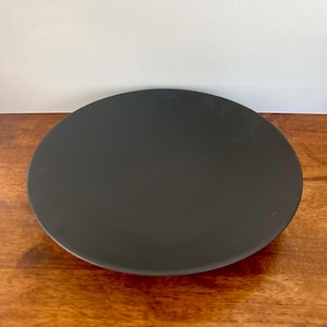 May include: A circular, matte black plate with a smooth, flat surface and a slightly raised edge. The plate features a solid, dark charcoal color throughout its entire top surface, presenting a clean and simple design for dining purposes.