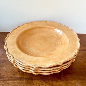 May include: A stack of four beige ceramic plates with a scalloped edge. The plates have a slightly textured surface and a shallow, rounded center. The plates are stacked on top of each other, showcasing their design.