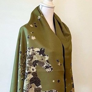 May include: A green scarf with a floral pattern and a black and white horse design. The scarf has a black border and a fringe.