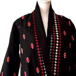 May include: Black embroidered jacket with red, white, and blue geometric patterns. The jacket has a long, open front and long sleeves.