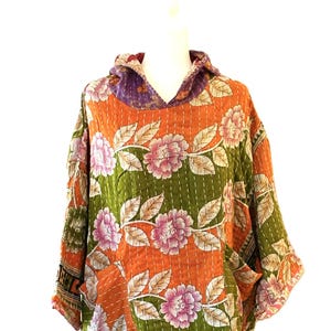 May include: A colorful, floral-patterned hoodie in orange, green, and pink. The hoodie features a hood and pockets, with a patchwork design and intricate stitching. The floral pattern includes large pink flowers and green leaves.