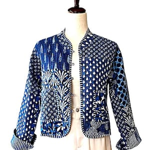 May include: A blue and white patterned jacket with a mandarin collar and three small buttons. The jacket features various geometric and floral designs in shades of blue and white. The sleeves are cuffed, and the jacket is displayed on a mannequin.