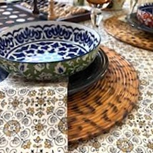 May include: A table setting featuring a patterned tablecloth, a blue and white patterned bowl, and a woven placemat. Other items include a black plate, glassware, and a tray with chess pieces.
