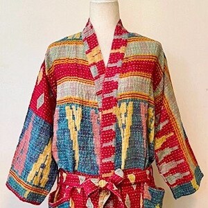 May include: A long-sleeved robe featuring a vibrant patchwork pattern in shades of red, blue, yellow, and white. The garment includes a matching tie belt at the waist, two front pockets, and a visible kantha-style running stitch texture throughout.