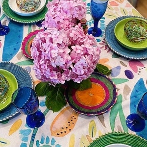 Könnte beinhalten: Eine weiße Tischdecke mit einem Aquarell-Blumenmuster. Die Tischdecke ist mit Tellern, Schalen und Gläsern gedeckt. Rosafarbene Hortensien stehen in der Mitte des Tisches.