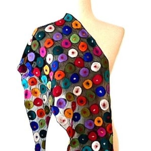 May include: A colorful scarf with a black mesh base, adorned with vibrant, circular, felted wool accents in various colors. The scarf is draped over a mannequin, showcasing its design and texture. Tassels hang from the ends.