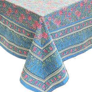 May include: A blue floral tablecloth with a repeating pattern of pink roses and green leaves. The tablecloth has a border with a geometric design. The fabric is draped over a table, showcasing the pattern and texture.