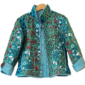 May include: A quilted jacket with a floral print in shades of green, blue, and white. The jacket has a mandarin collar, a button closure, and long sleeves.