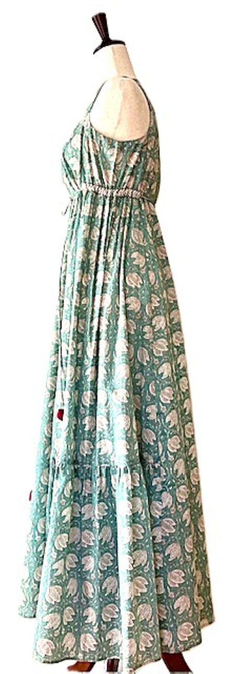 Puede incluir: Un vestido maxi largo y fluido de color verde con estampado floral blanco. El vestido tiene un escote halter y un lazo en la cintura.