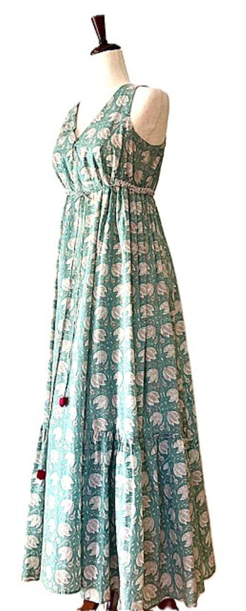 Puede incluir: Un vestido maxi sin mangas con escote en V y estampado floral. El vestido tiene un lazo en la cintura y una falda de capas.