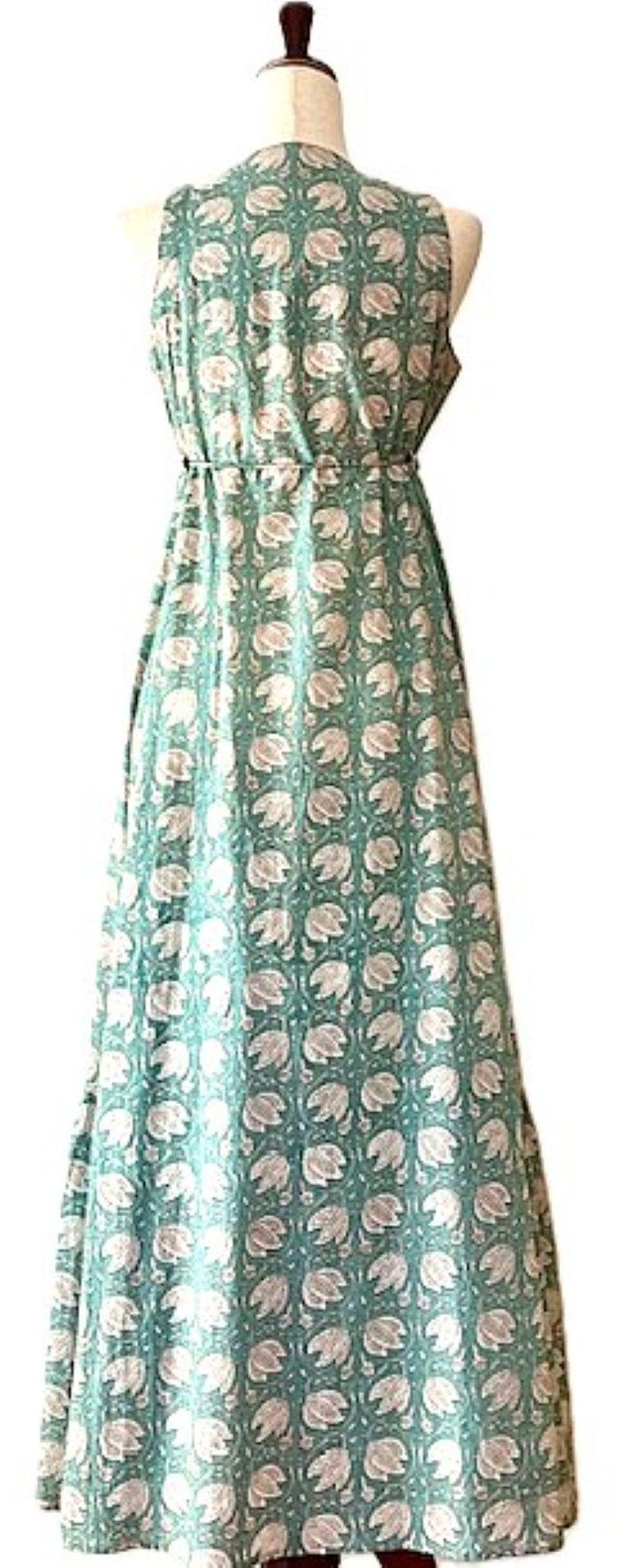 Puede incluir: Un vestido maxi sin mangas con fondo verde y estampado floral blanco. El vestido tiene un escote en V y un lazo en la cintura.